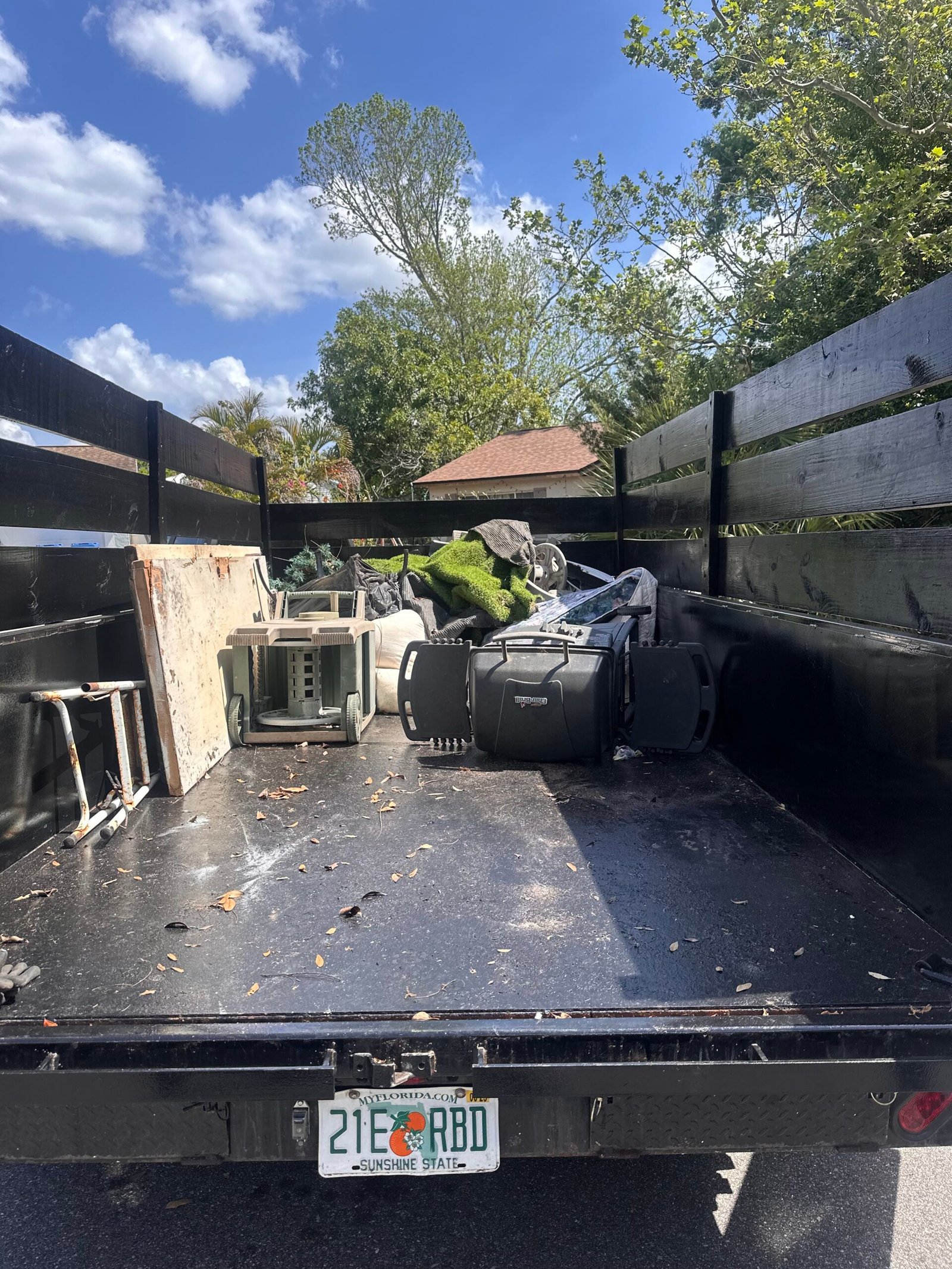 Rear view into a black trailer with mixed contents, a wood panel and overturned chairs