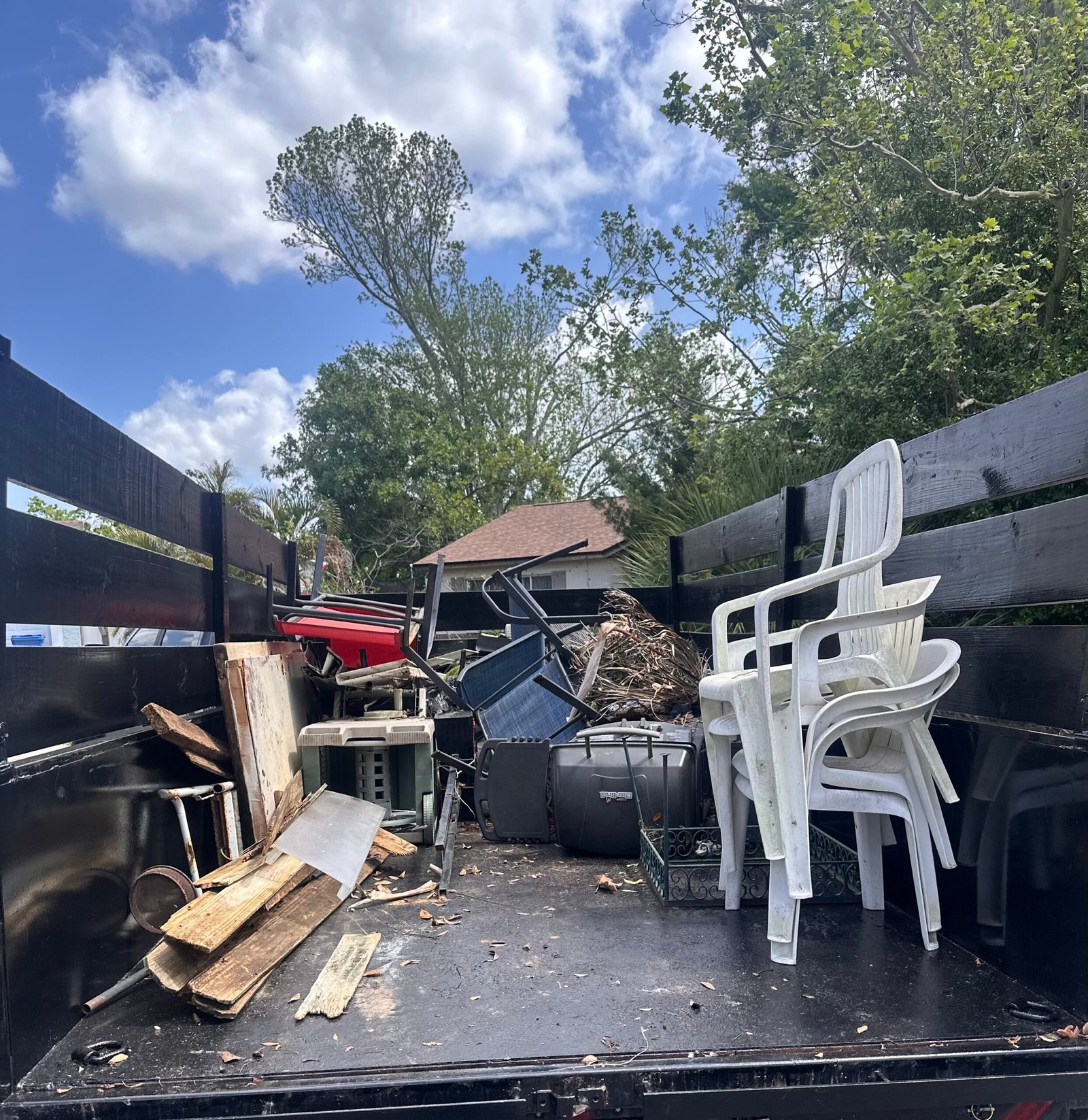 Stacked white chairs, frames and wood pieces inside a black-sided trailer