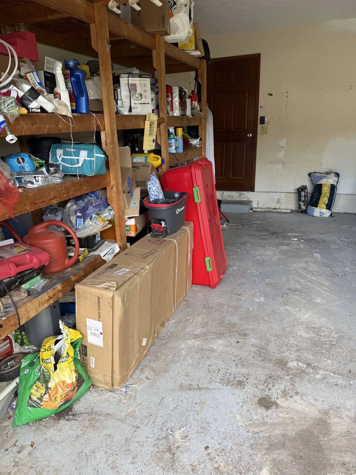Open garage walkway beside wooden shelving holding stored household items.